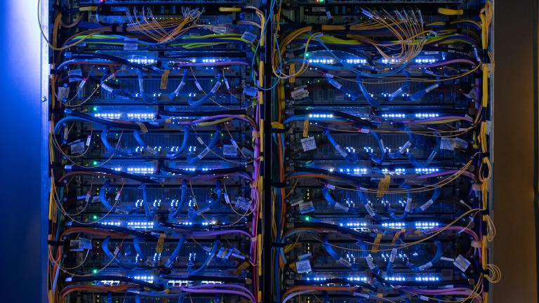 two blue racks of computer chips and servers, connected by yellow cords