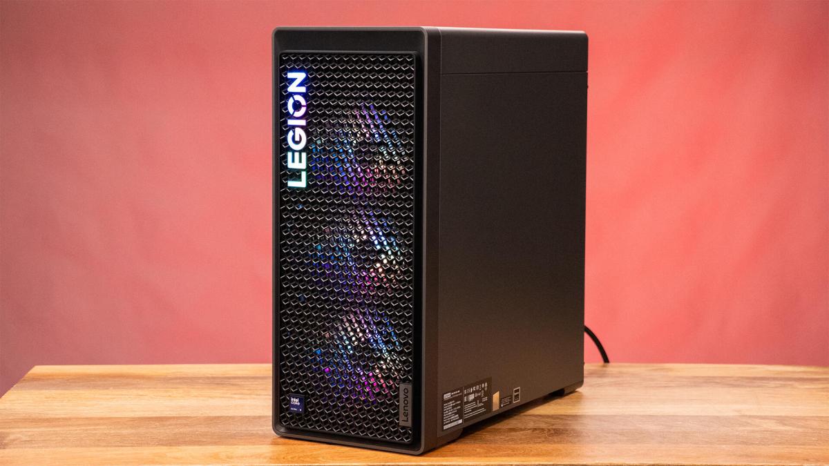 Um PC desktop preto em cima de uma mesa de madeira em frente a um fundo vermelho.
